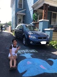 A Young Scholar poses with a picture of the whale she drew in her home's driveway.