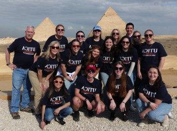 Students and 教师 wearing Utica t-shirts stand in front of the pyramids during a January 2023 trip to 埃及.
